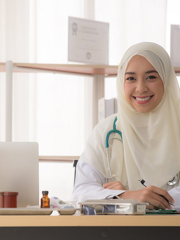 Portrait of charming muslim female doctor working at office desk and smiling at camera