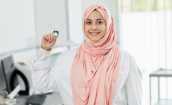Waist up portrait of young Middle-Eastern woman working as nurse in medical clinic and smiling at camera holding bottle of pills, copy space